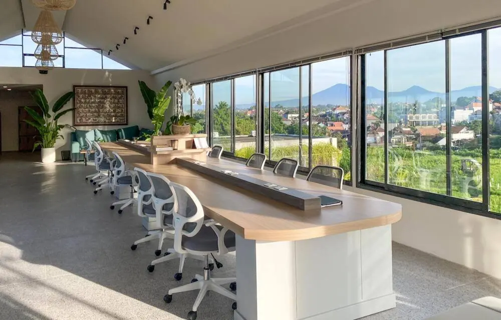 A long shared desk beside floor-to-ceiling windows with a view of the mountains