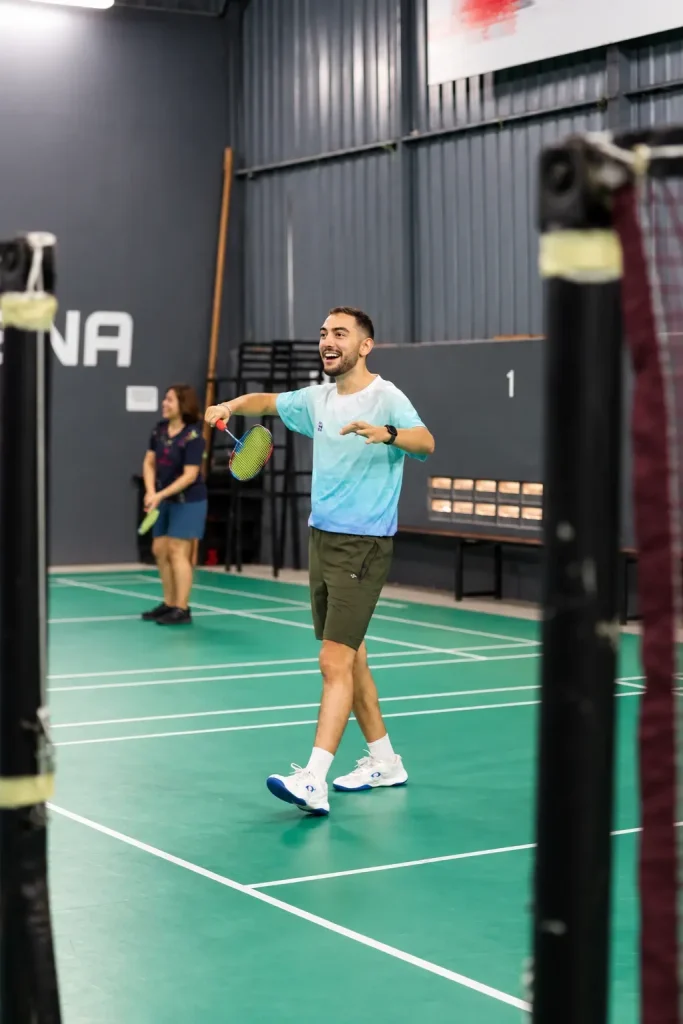 A player laughing mid-rally on an indoor badminton court