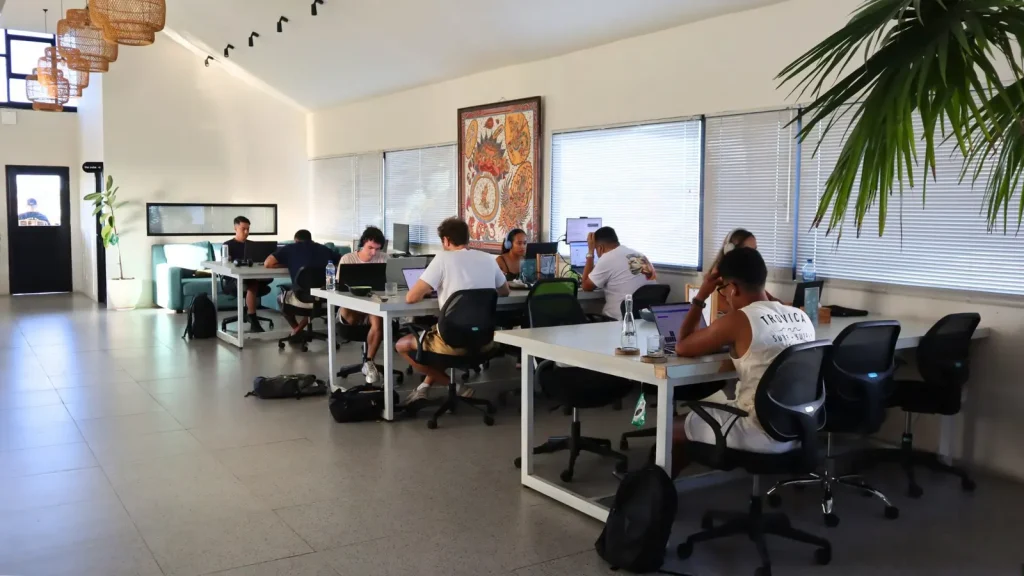 Members at work in a bright room of white desks under a Balinese painting