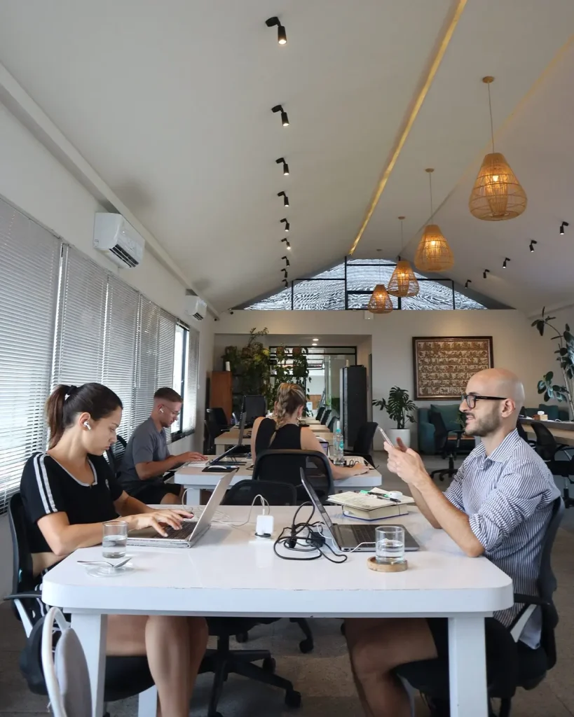 Members working and chatting at a shared table under the hall's rattan lamps