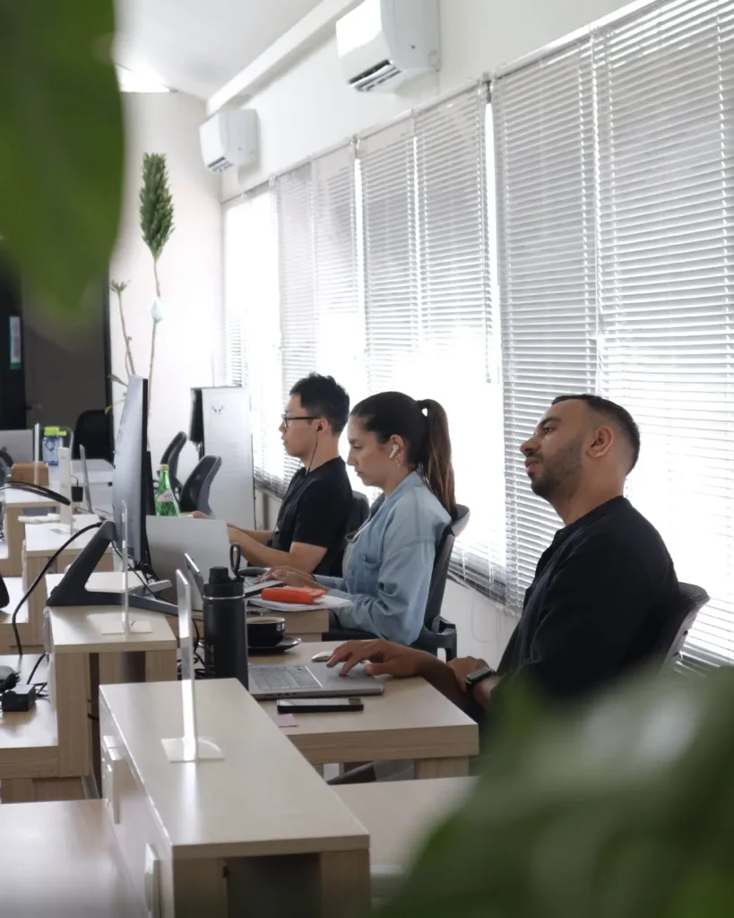 Three members working side by side at a long desk by the window