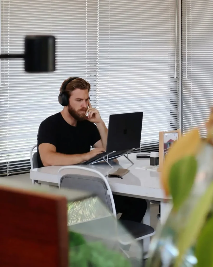 A member in headphones working on his laptop by the window