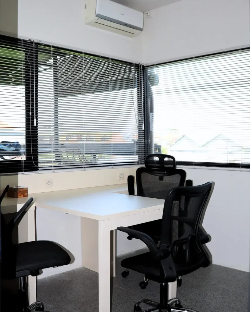 A corner desk with ergonomic mesh chairs by the window