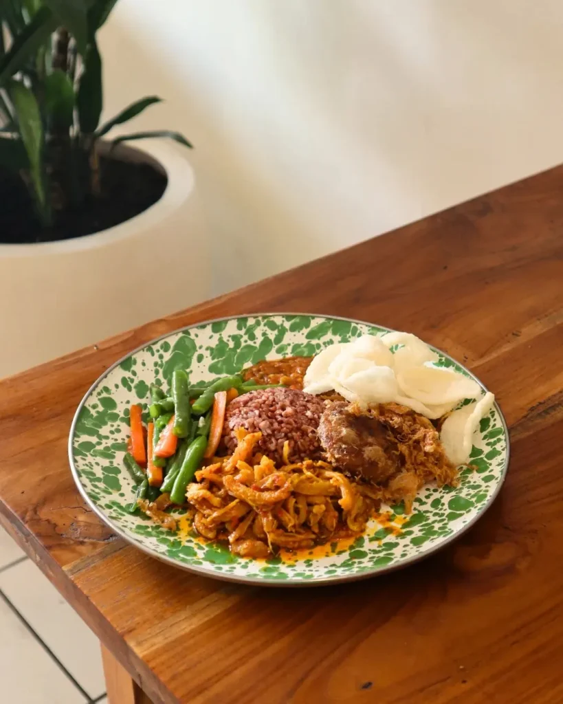 Nasi campur with red rice, vegetables and crackers